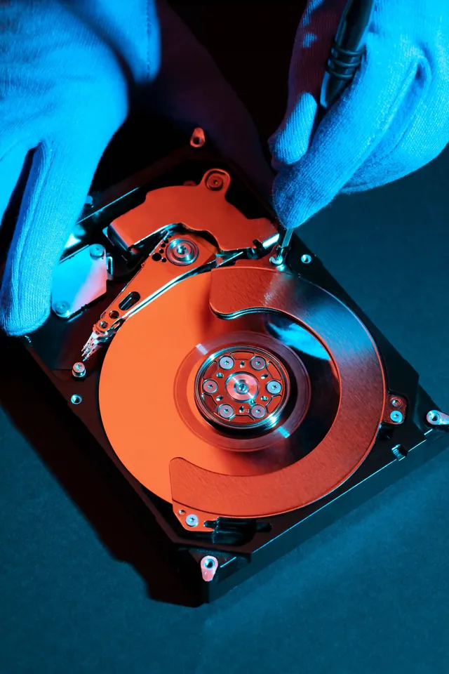 Gloved hands working on an open hard disk drive